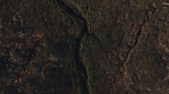Aerial top down view of a winding stream cutting through dark peat moorland.