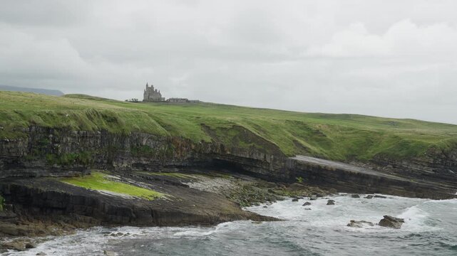 Wide view of Classiebawn Castle above layered sea cliffs and a rocky Atlantic shoreline at Mullaghmore Head in County Sligo, Ireland, under overcast skies.