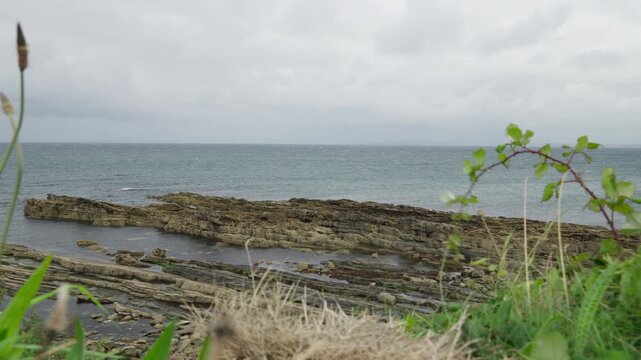 Ground-level coastal view of exposed layered rock and tidal pools beside the Atlantic Ocean at Mullaghmore Head in County Sligo, Ireland, beneath cloudy skies.