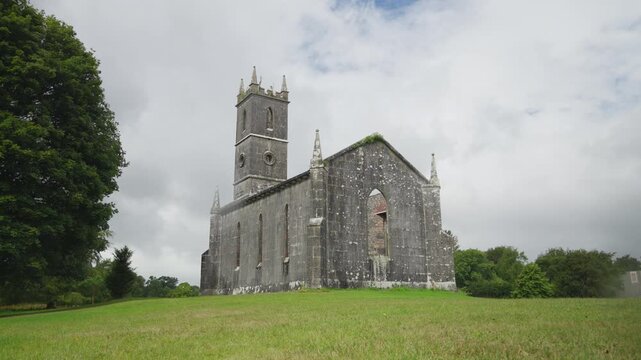 The roofless 1833 Church of Ireland building at Rockingham Demesne shows limestone walls, lancet windows and a crenellated tower near Lough Key.