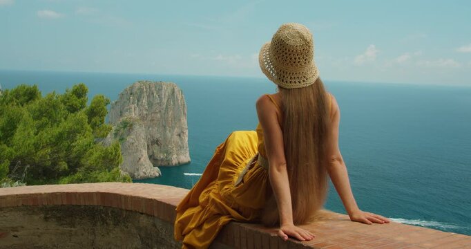 Woman relaxing at Capri viewpoint above blue sea and Faraglioni cliffs in summer