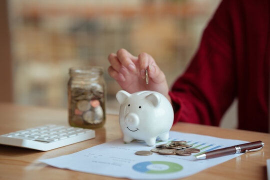 The close-up image shows a young woman planning her personal finances at home, using a piggy bank, calculator, and coins&mdash;symbols of saving, budgeting, investing, income, and future financial security.
