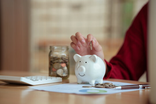 The close-up image shows a young woman planning her personal finances at home, using a piggy bank, calculator, and coins&mdash;symbols of saving, budgeting, investing, income, and future financial security.
