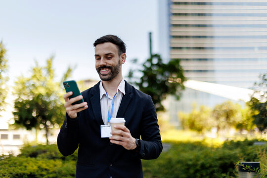 Businessman smiling while checking smartphone and drinking coffee