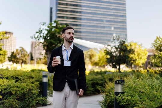 Young professional man walking through urban park, holding coffee
