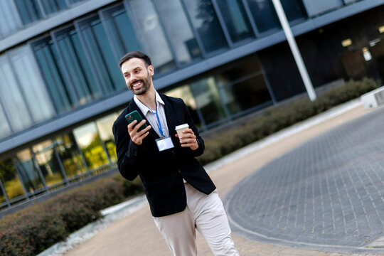 Confident businessman walking outside office building checking phone