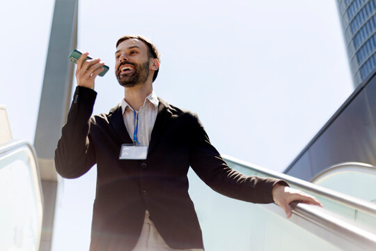 Professional man speaking voice message on smartphone ascending escalator