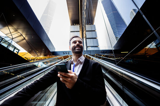 Professional man using smartphone on modern escalator