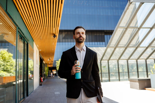 Professional man walking in city street holding reusable bottle