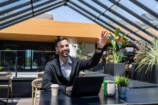 Happy businessman waving hand at modern cafe