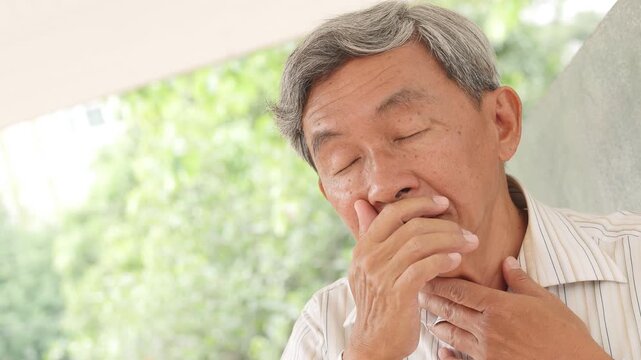 elderly asian man with silver hair experiencing throat pain outdoors, coughing and uncomfortable, outdoor park scene