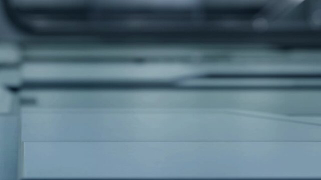A printer is working in an office space. The machine is producing documents. The environment is busy with typical office items around. It is a regular workday.