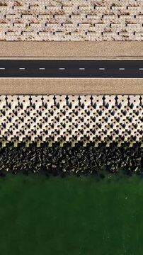 Aerial top-down view reveals patterned dike pavement road and rocky breakwater beside green water at Breezanddijk Netherlands