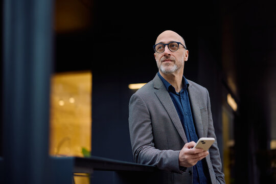 Mature businessman with cell phone in city looking away,