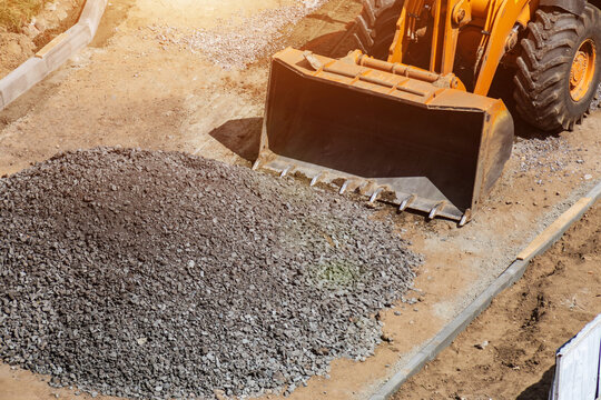 Heavy duty orange wheel loader with large front bucket positioned next to extensive pile of crushed stone and aggregate on outdoor construction site under bright sunlight, copy space