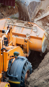 Orange construction loader bucket full of soil engaged in earthwork at construction site during day, heavy machinery in action moving ground for foundation work, vertical photo