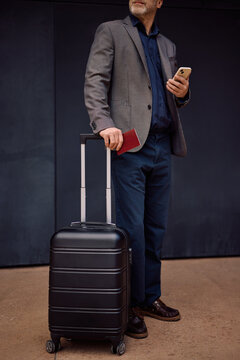 Unrecognizable business traveler with passport and suitcase.