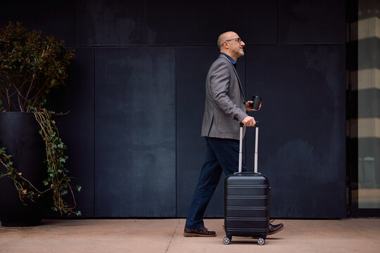 Businessman with travel bag and takeaway coffee walking on street.