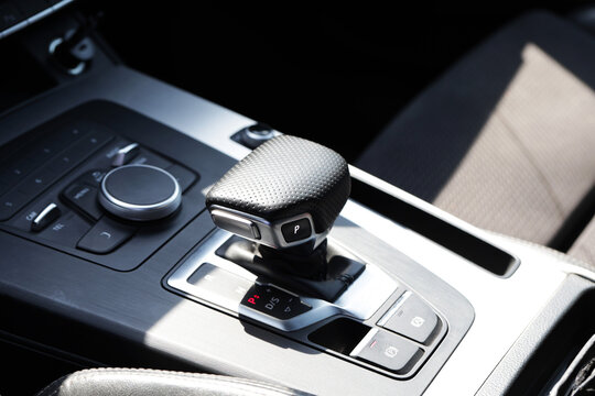 Car interior view showing automatic transmission gear selector with illuminated park indicator, brushed aluminum accents, and modern infotainment controls under bright daylight
