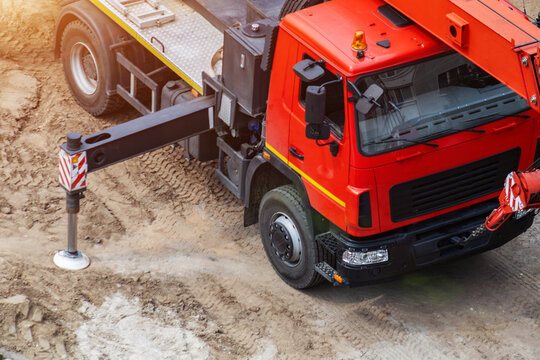 Red truck crane with extended outrigger stabilizer on dusty construction ground, heavy vehicle for lifting material on building site, engineering machinery work, copy space