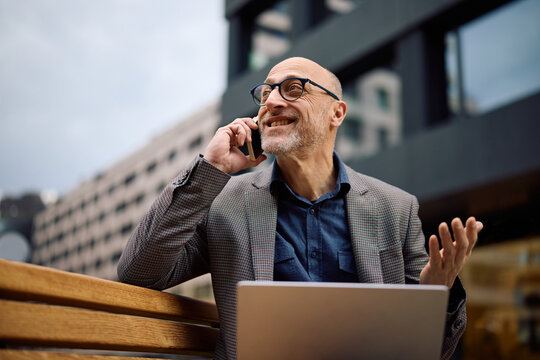 Happy entrepreneur making phone call while using laptop outdoors.