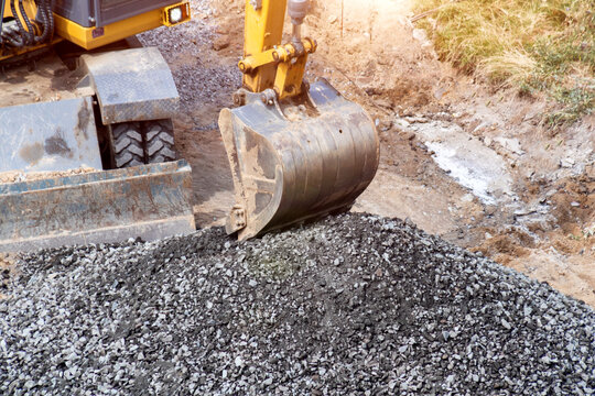 Excavator bucket moving crushed stone material, heavy machinery at construction site, earthmoving equipment for roadwork, industrial vehicle operation handling aggregate, copy space