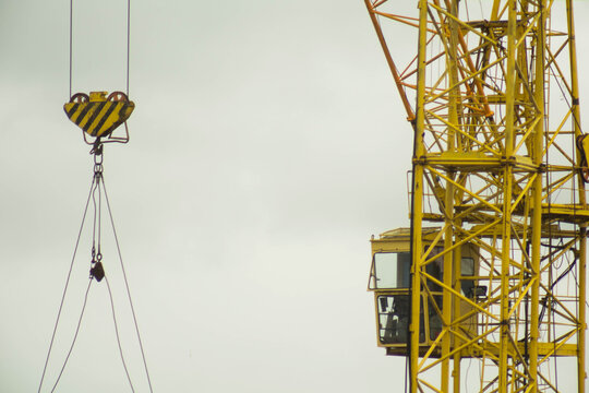 Yellow tower crane boom and operator cabin against overcast sky, machinery for lifting heavy materials on construction site of multistory building