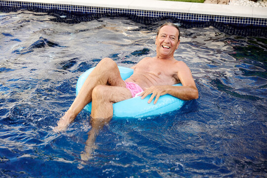 Senior man relaxes on an inflatable ring in a home swimming pool
