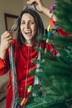 Smiling woman in red shirt decorates a Christmas tree indoors