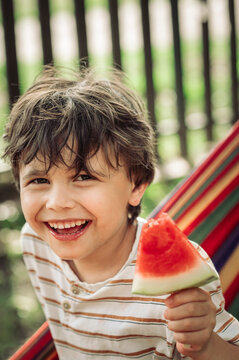 A smiling boy holds a fresh watermelon slice outdoors in summer