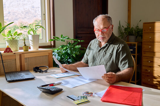 A man reviews financial documents at a desk in his home office