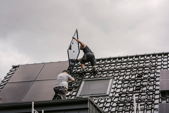 Workers install a solar panel on a tiled roof for modernization