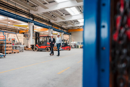 Two men wearing hard hats walking and talking in factory shop floor