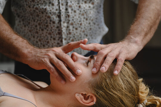 Male osteopath gives facial massage to female patient indoors