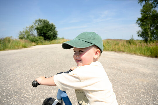A smiling boy rides a balance bike outdoors on a sunny summer day