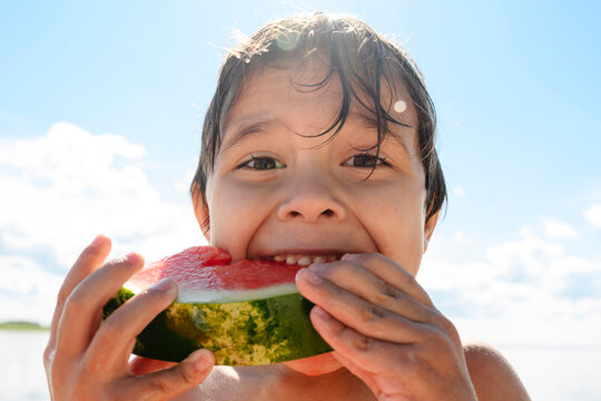 Happy boy eating a slice of watermelon outdoors in summer