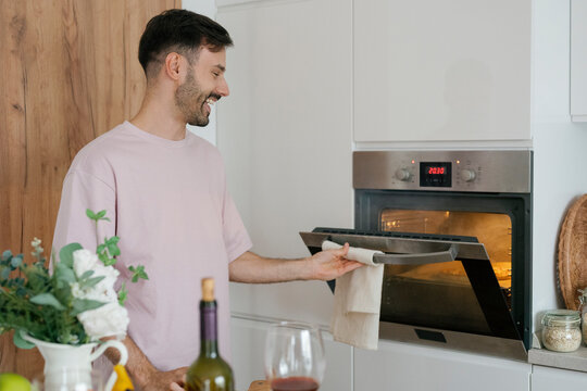 Cheerful person opening oven making pizza in modern kitchen