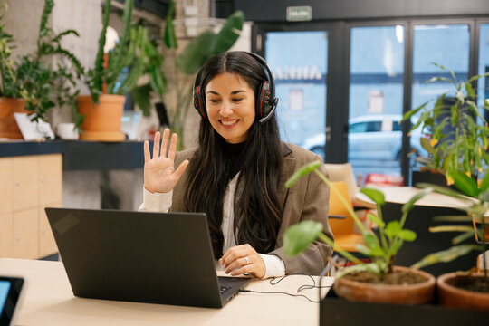 Businesswoman with headset waving during video call in coworking office