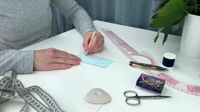 The woman draws straight lines on the skirt pattern; the lady is learning the basics of sewing at home. The concept of learning sewing skills and taking the first steps in handicrafts, midsection