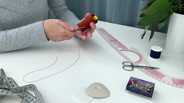 The woman measures thread from the spool and cuts it with tailor&rsquo;s nippers, shears; the creative process of making unique clothing according to her own design, a home workshop, a hobby
