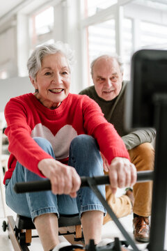 Smiling woman exercises on a rowing machine with a male teacher