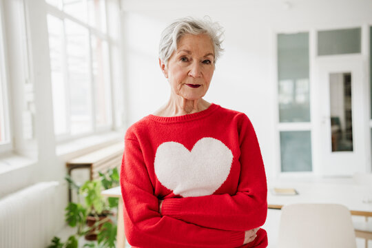 Confident woman wears a red heart sweater in a bright room