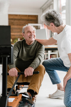 Woman supports man exercising on rowing machine indoors