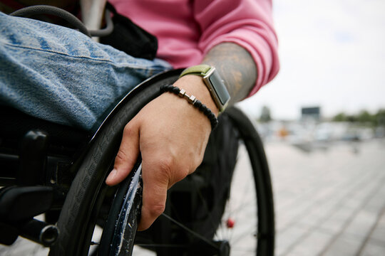 Male hand pushes a wheelchair wheel outdoors in the city