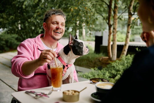 Man in wheelchair enjoys coffee with female friend and dog at cafe