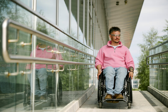 Man in wheelchair uses an accessible ramp outside a glass building