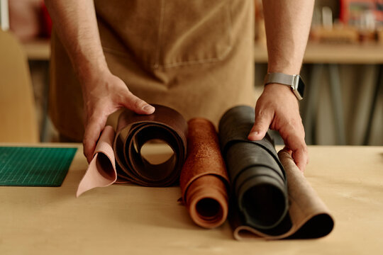 Unrecognizable artisan choosing genuine leather rolls on table