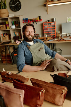 Smiling male artisan sits at workbench in his leather workshop