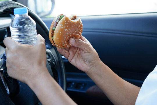 Asian woman driver hold and eat hamburger in car, dangerous and risk an accident.