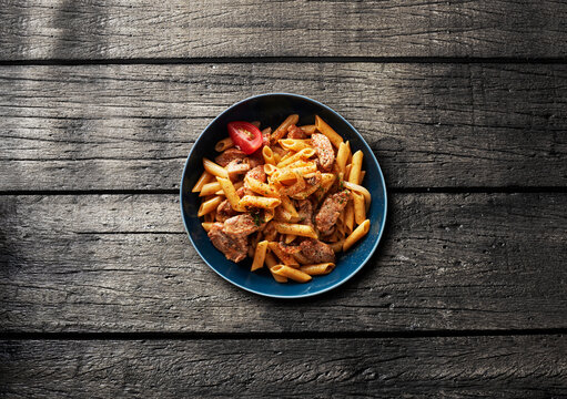 A blue bowl contains penne pasta with meat and tomato sauce
